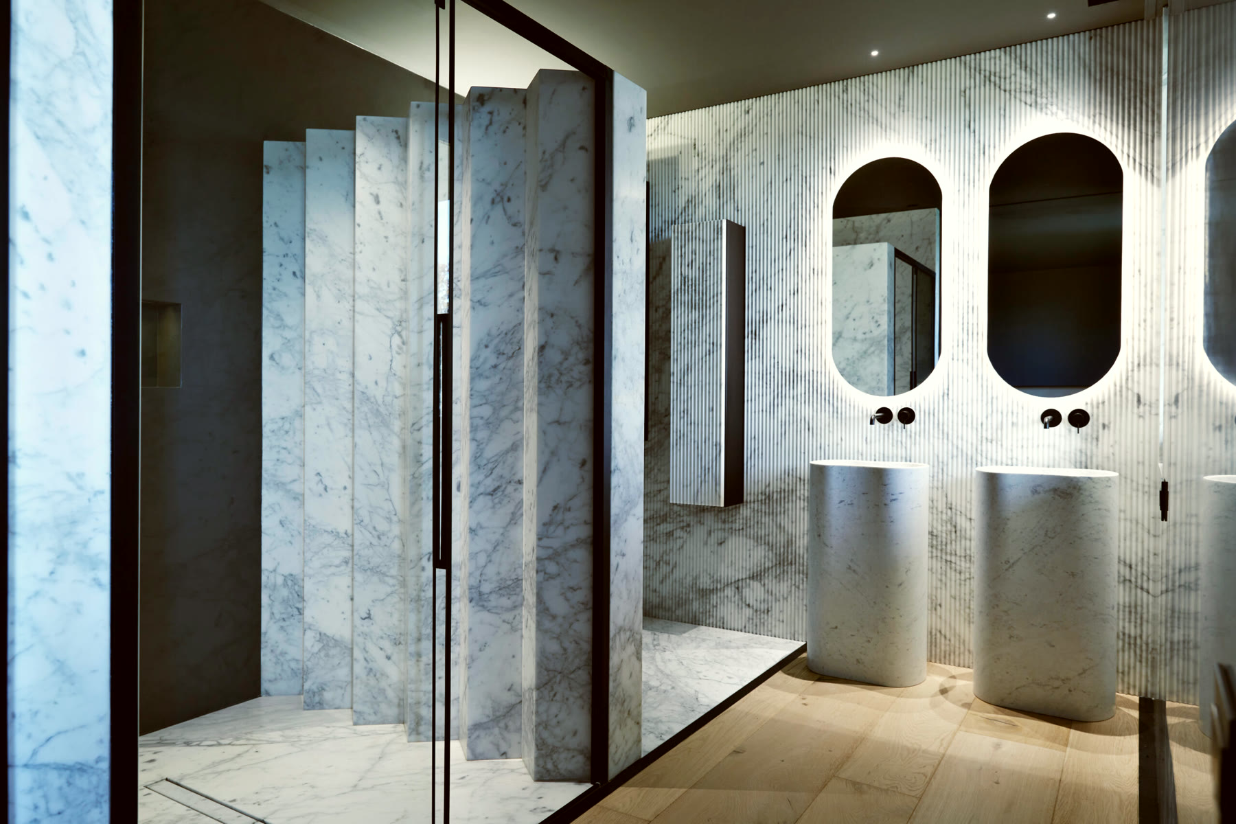 Bad aus Carrara-Marmor mit zwei Säulenwaschbecken und beleuchteten Bogenspiegeln
